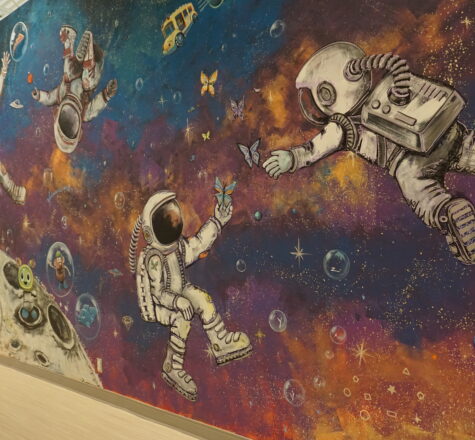 A colourful space-themed mural image in purple, orange, blue with astronauts in various poses alongside well-known toys, objects and devices used during therapy sessions at KidsAbility.